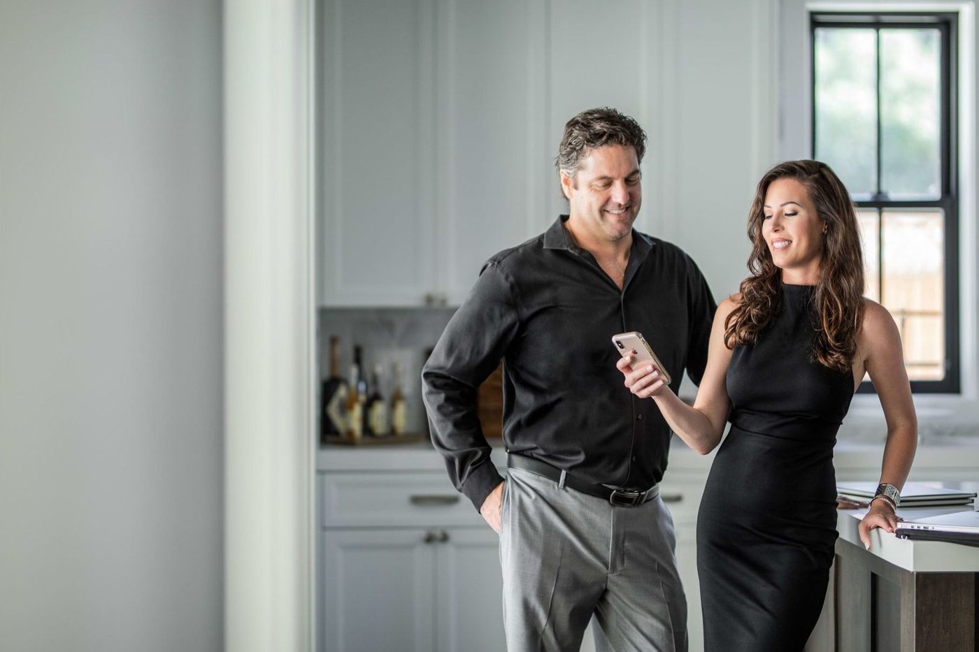 Couple in black outfits looking at phone in a bright kitchen