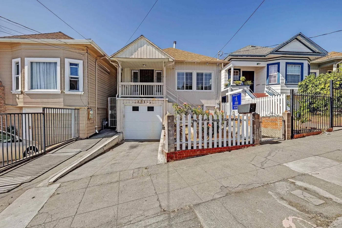 Tan house with white picket fence and neighboring homes on a street